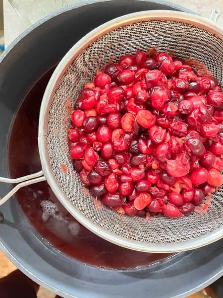 Cranberries after boiling in a fine mesh strainer over top to a large stockpot to catch the cranberry juice.